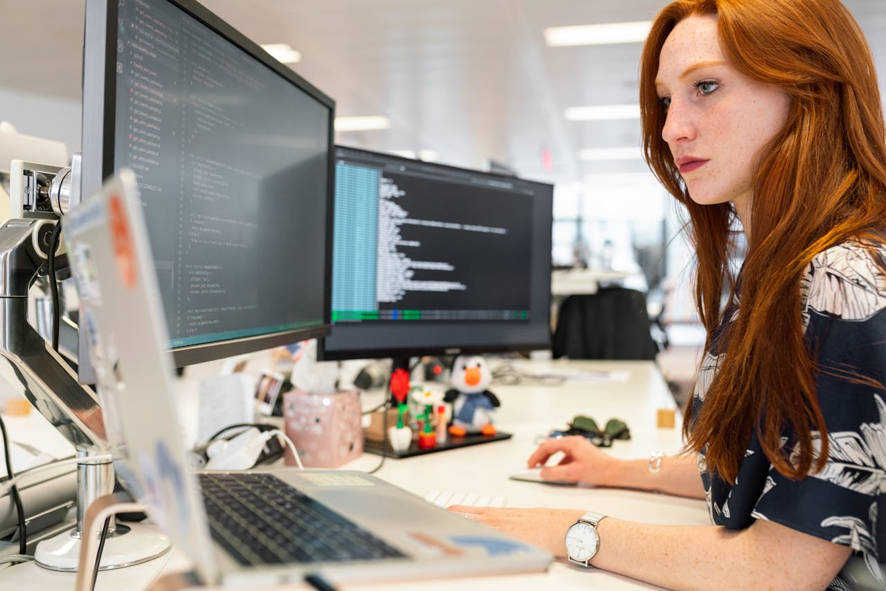 Woman working on computer with multiple screens.